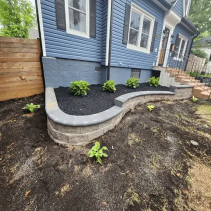Curved stacked-block retaining wall with a capped top edging a fresh mulch bed of young shrubs