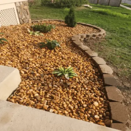 River-rock ground cover behind a curved stone block border with small plantings and lawn beyond