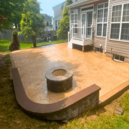 Stamped concrete patio with a round stone fire pit and a curved seat wall behind a house
