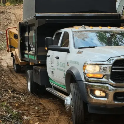 White dump-body work truck with a yellow wood chipper on a dirt access road